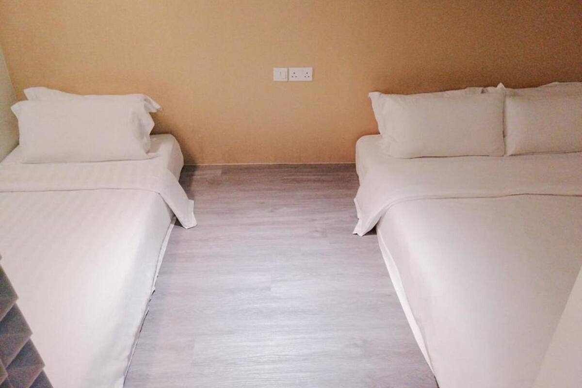 A room with two beds, a wooden floor, and a plain beige wall.