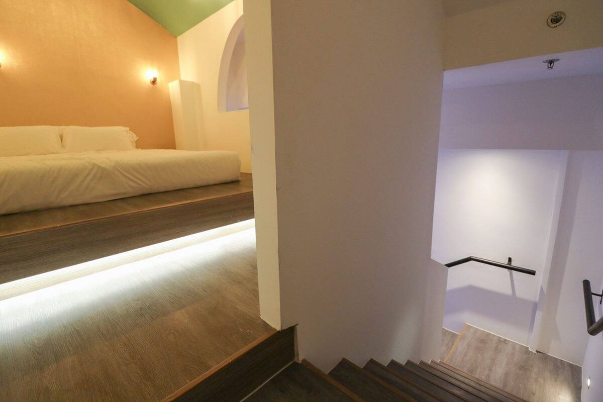 A modern hotel room with a wooden floor, a bed, and a staircase with a handrail.
