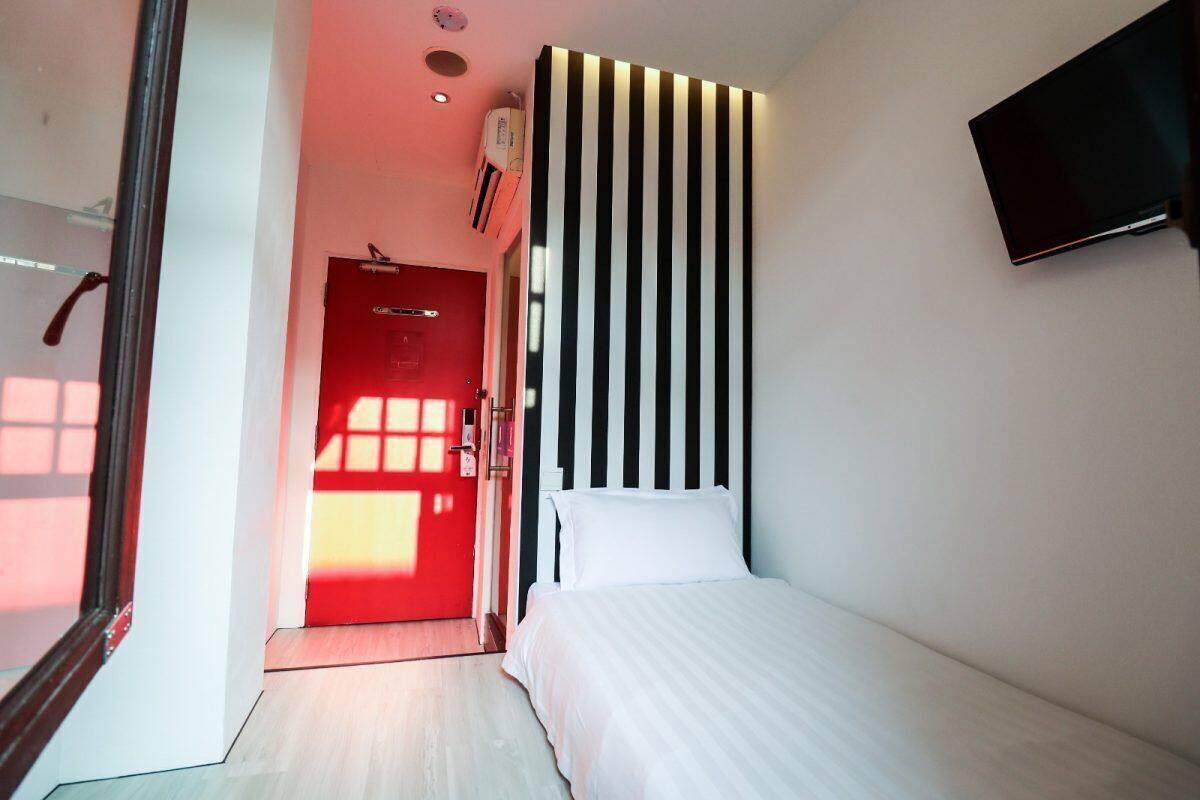 A modern hotel room with a bed, a red door, and a wall-mounted TV.