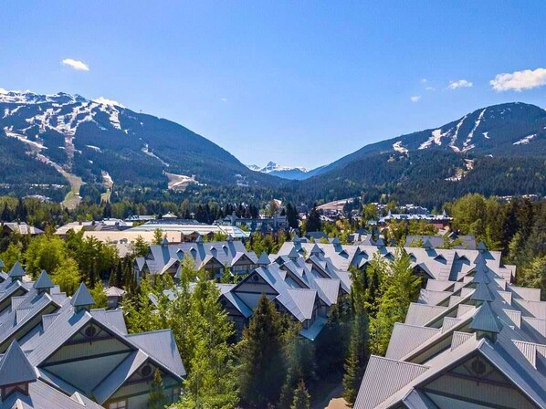 A resort with multiple chalet-style buildings, a ski slope in the background, and a mountainous landscape.