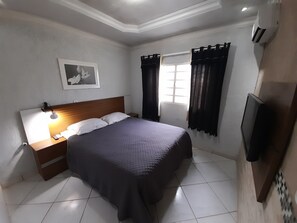A neatly arranged bedroom with a bed, bedside table, lamp, and a framed picture on the wall. - Exclusive Pool (Planaltina)