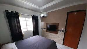 A bedroom with a bed, a TV mounted on the wall, a door, and a window with curtains. - Exclusive Pool  (Planaltina)
