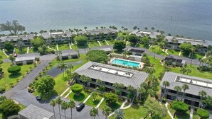 Une vue aérienne d’un complexe hôtelier comprenant plusieurs bâtiments, une piscine et une grande étendue d’eau en arrière-plan.