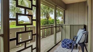 Un espace extérieur abrité doté d’un sol à motifs, d’une chaise avec un coussin à motifs et d’une vue sur des palmiers et une végétation luxuriante.