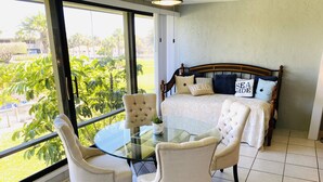 Une chambre à coucher avec un lit, une table en verre et des chaises, et une vue sur la verdure à l’extérieur.