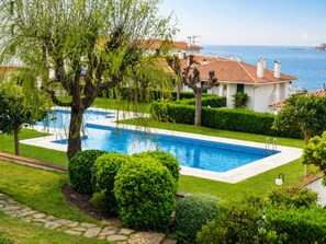 Ein Swimmingpool, umgeben von gepflegter Bepflanzung, mit Blick auf das klare Meer und ein traditionelles Gebäude mit Ziegeldach.
