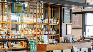 A bar area with a tiled backsplash, wooden shelves, and a variety of bottles and glasses. - Palace Hotel Mortlake (Mortlake)