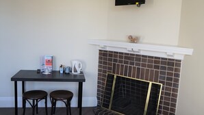 A room with a fireplace, a table with two chairs, and a mounted television. - Palace Hotel Mortlake (Mortlake)