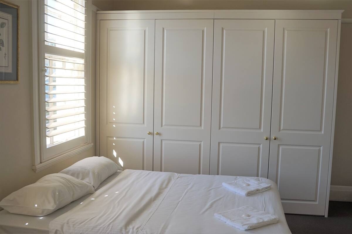 A bedroom with a bed, white curtains, and a wardrobe.