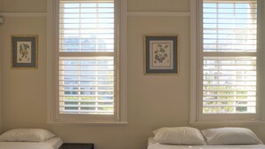 A bedroom with two beds, large windows with blinds, and framed artwork on the walls. - Palace Hotel Mortlake (Mortlake)
