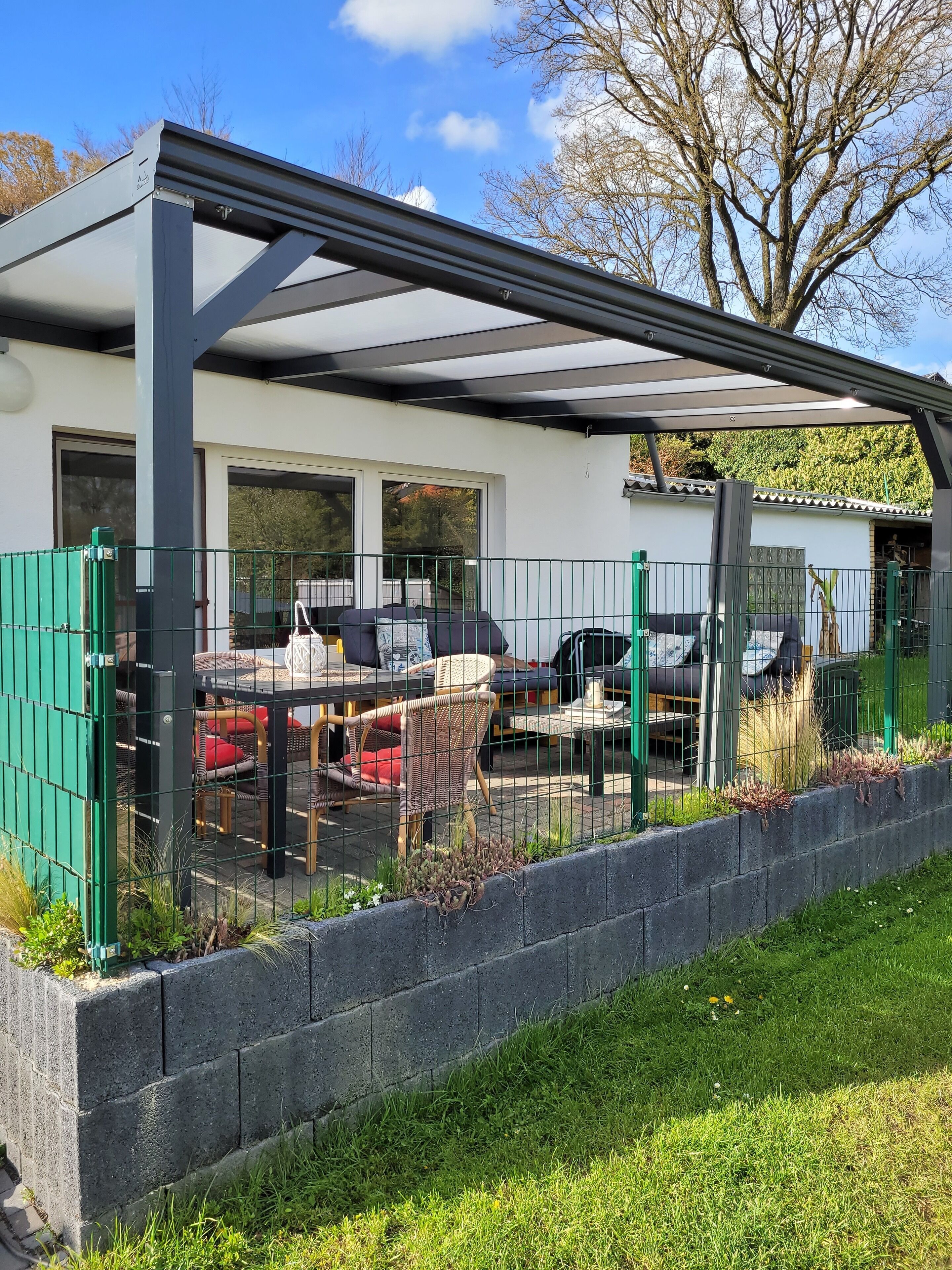 Un'area patio coperta con mobili da esterno, un'auto e un recinto verde.