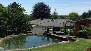 A patio area with a brick floor, a wooden table, and a small pond. - Moni's chicken farm Pure nature Outdoor pool for shared use (Nettetal)