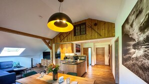 Een ruime loft met houten inrichting, een eethoek met een houten tafel, een keuken met houten kastjes en een groot raam.