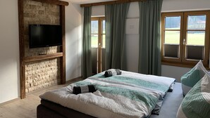 Ein Schlafzimmer mit Backsteinwand, Flachbildfernseher, Bett mit gestreifter Bettwäsche und großen Fenstern mit Vorhängen.