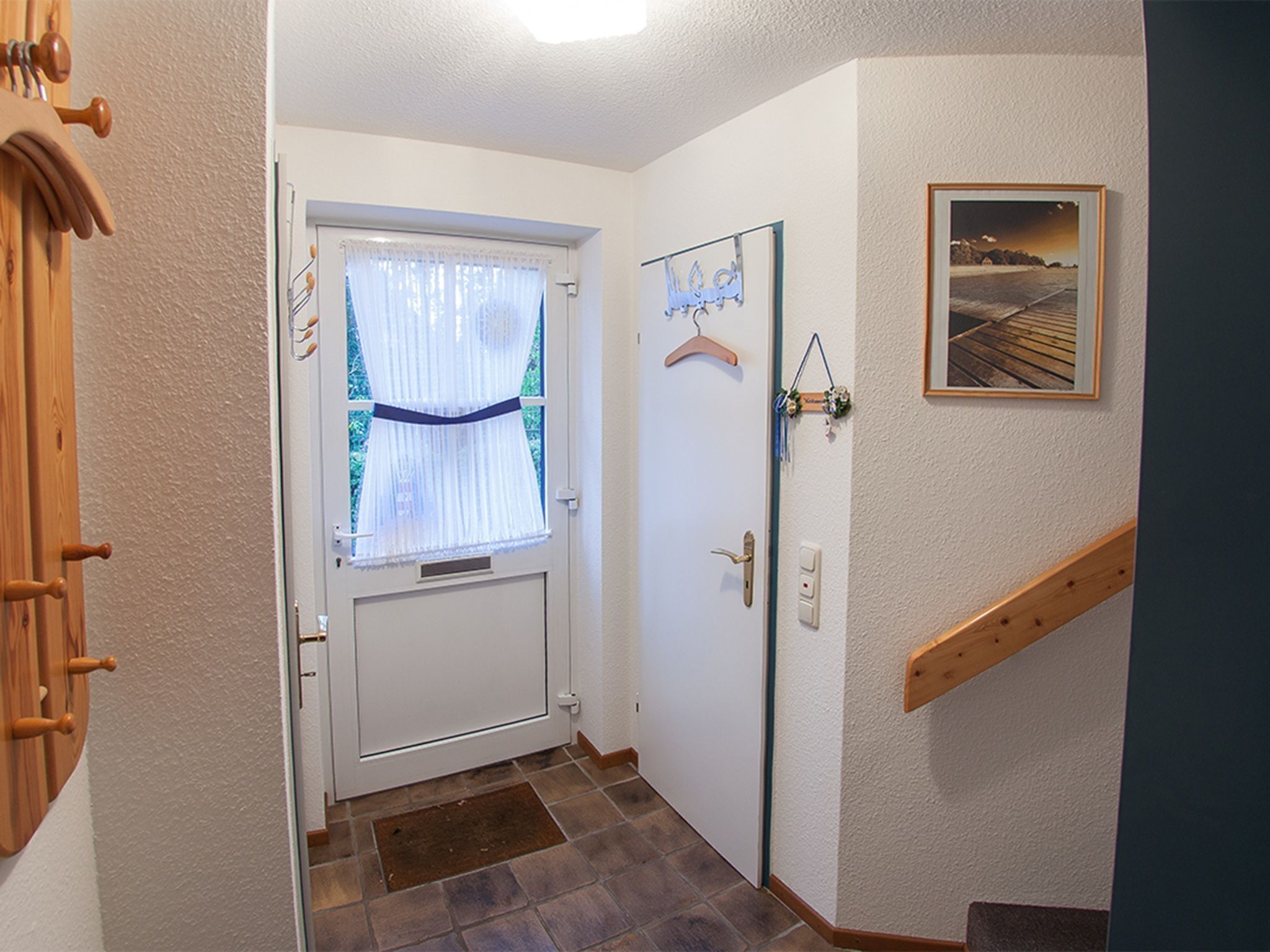 Un couloir avec une porte blanche, un escalier en bois et un tableau encadré accroché au mur.