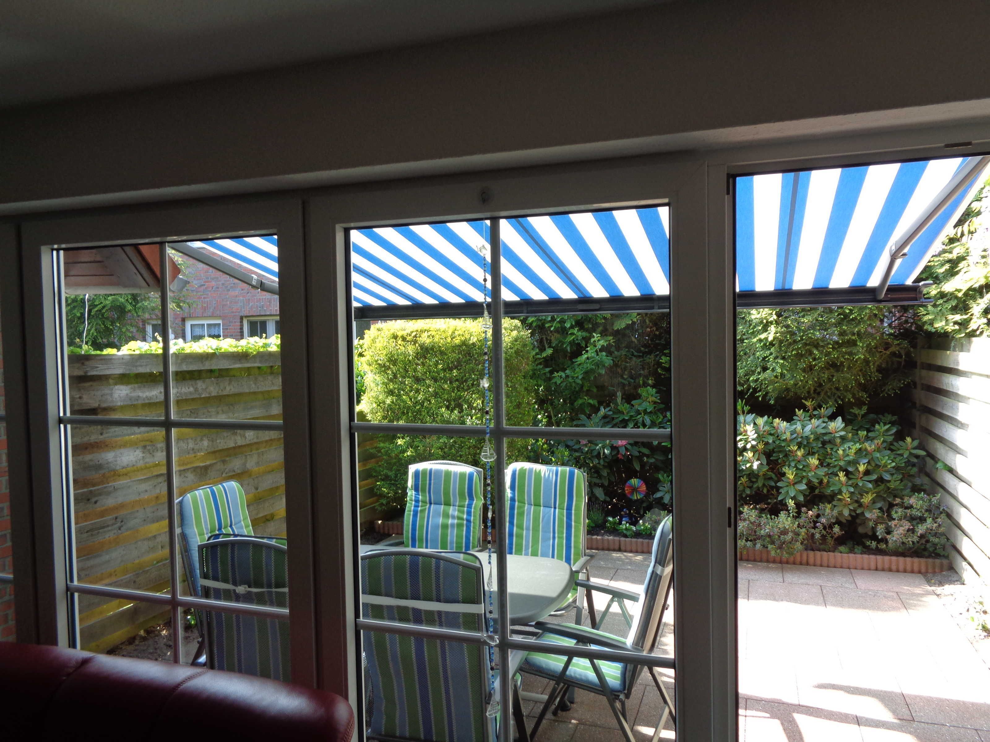 Un espace patio avec des chaises à rayures et une table, un auvent bleu et blanc à rayures, et une vue sur un mur de briques et de la verdure.