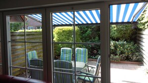Een patio met gestreepte stoelen en een tafel, een blauw-wit gestreept zonnescherm, en uitzicht op een bakstenen muur en begroeiing.