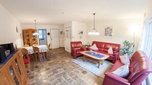 Een woonkamer met een rode bank, een salontafel en een eethoek met een tafel en stoelen.