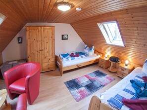 A cozy attic bedroom with a sloped ceiling, wooden walls, a single bed, a red chair, a small desk, and a window. - Ferienhaus Kickler, Vermietungsservice Dangast - Ferienhaus Kickler (Varel)