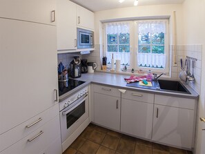 Una cocina con armarios blancos, microondas, estufa, fregadero y ventana con cortinas.