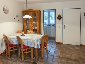 Un comedor con una mesa, sillas, un armario de madera y una cocina visible a través de una puerta de cristal.