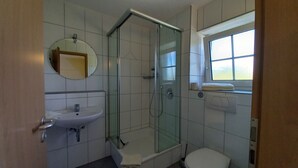 A bathroom with a glass-enclosed shower, a sink, a toilet, and a window. - Ferienhof Metzler 1 Zi. Appartement Apfel (Bodnegg)