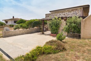 A house with a stone facade, a covered patio, and a garden with various plants and flowers. - Appartamento Nuraghe with Air Conditioning, Garden and Terrace (Gonnesa)