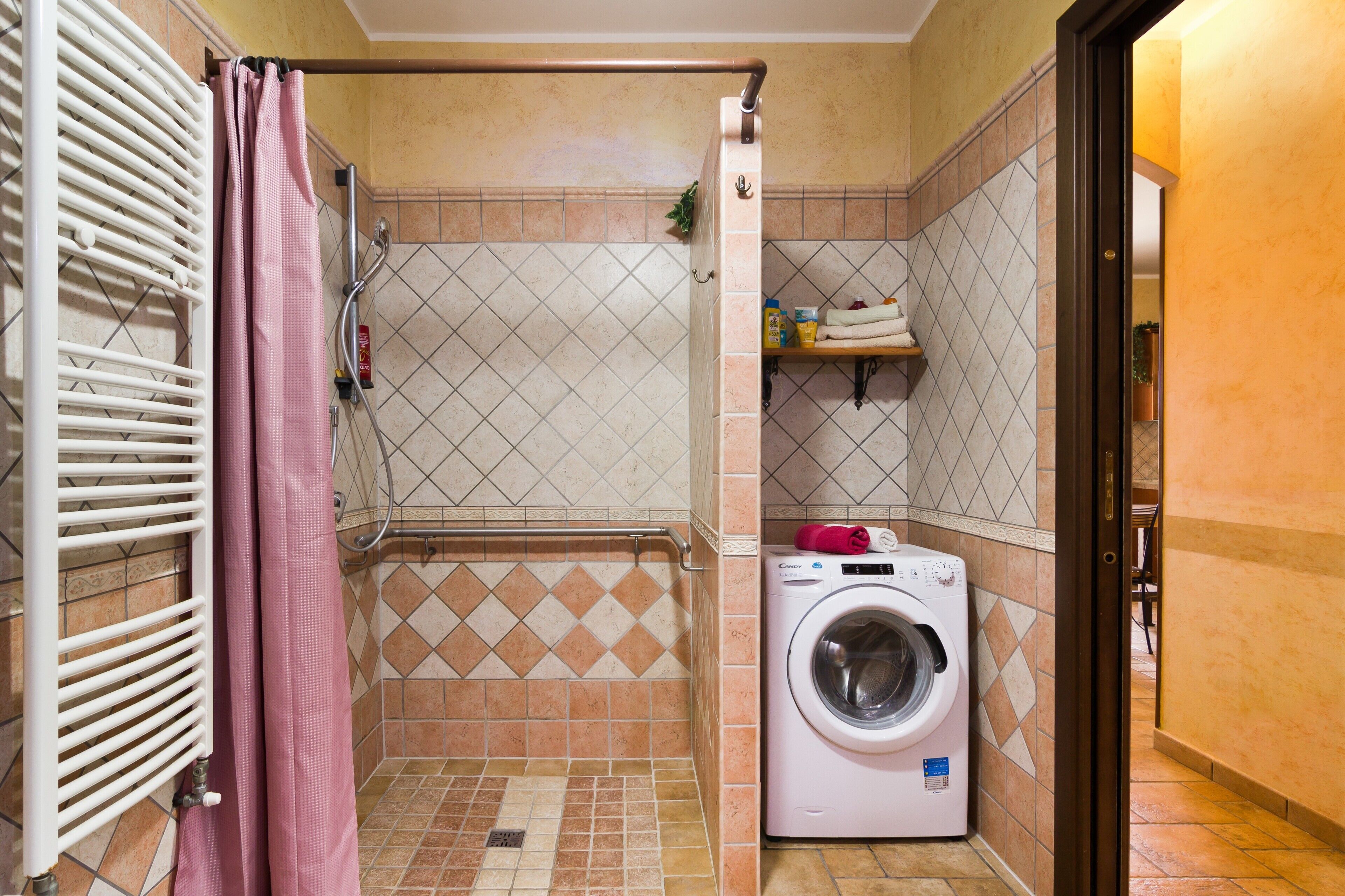 A compact bathroom with a shower, a washing machine, and a towel rack.
