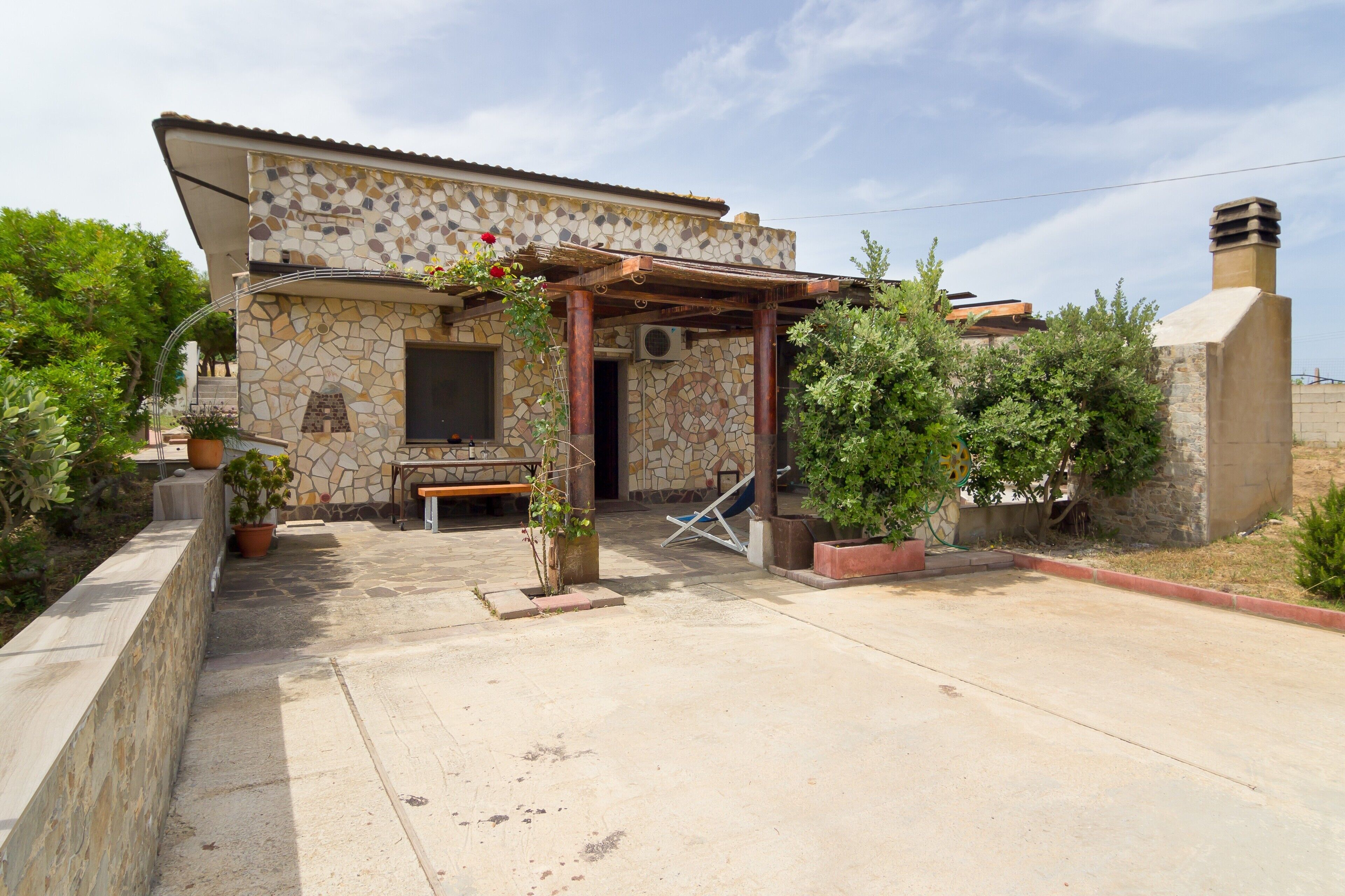 Una casa de piedra con un patio, una pérgola de madera y una chimenea.