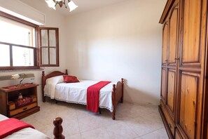 A bedroom with a bed, a wooden wardrobe, a desk with a lamp, and a window.