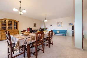 Un coin repas avec une table dressée pour quatre personnes, des chaises en bois, un buffet avec des portes en verre et, au fond, un canapé bleu.