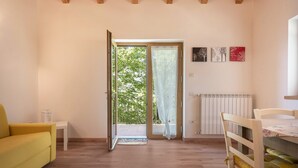 A room with a yellow sofa, a white table, a wooden chair, a radiator, and a door leading outside.