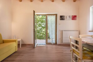Une pièce avec un canapé jaune, une table blanche, une chaise en bois, un radiateur et une porte donnant sur l’extérieur.