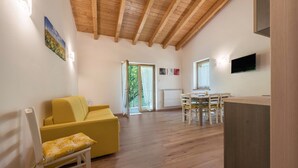 A spacious room with a wooden ceiling, a yellow sofa, a dining table with chairs, and a television mounted on the wall.