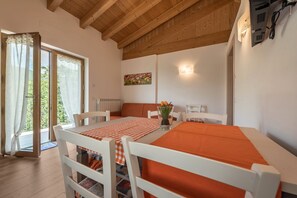 Un coin repas avec une table dressée pour quatre personnes, des chaises blanches, une nappe rouge et une vue sur l’extérieur grâce à une porte vitrée.