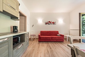 Ein gemütlicher Wohnraum mit einer Küchenzeile, einem roten Sofa, einem Esstisch und einem weißen Stuhl.
