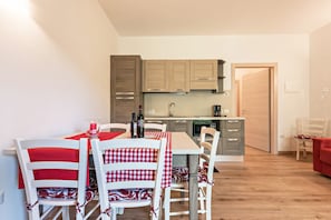 Une cuisine de taille réduite avec des meubles en bois, une table à manger recouverte d’une nappe à carreaux rouges et blancs, et des chaises blanches.