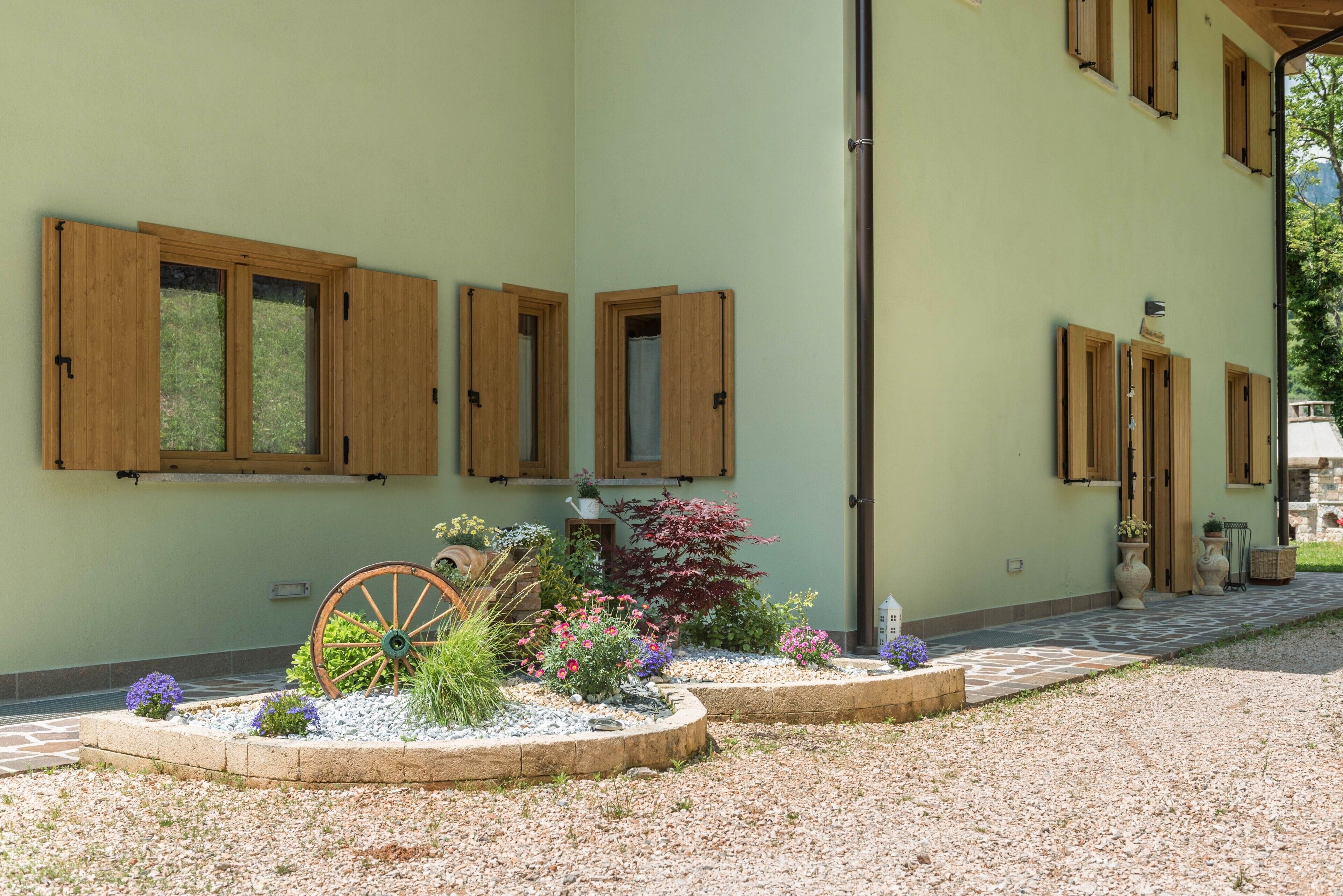 A building with multiple windows, a wheelbarrow, and a garden with various plants.