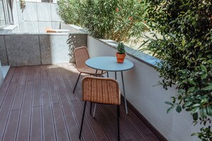 A small outdoor patio with a round table and two wicker chairs, surrounded by greenery and a stone wall. - STAY&CO Lisbon Marques de Pombal (Lisbon)