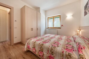 A bedroom with a wooden wardrobe, a window with curtains, and a floral bedspread.
