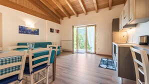 A spacious room with a wooden ceiling, a dining area with checkered tablecloths, a sofa, and a kitchen with cabinets and a sink.