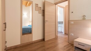 A room with a wooden floor, a bed with a blue bedspread, a wooden wardrobe, and a mirror on the wall.