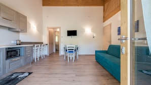 A modern kitchen with a dining area, a TV mounted on the wall, and a teal sofa.