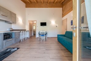 A modern kitchen with a dining area, a TV mounted on the wall, and a teal sofa.