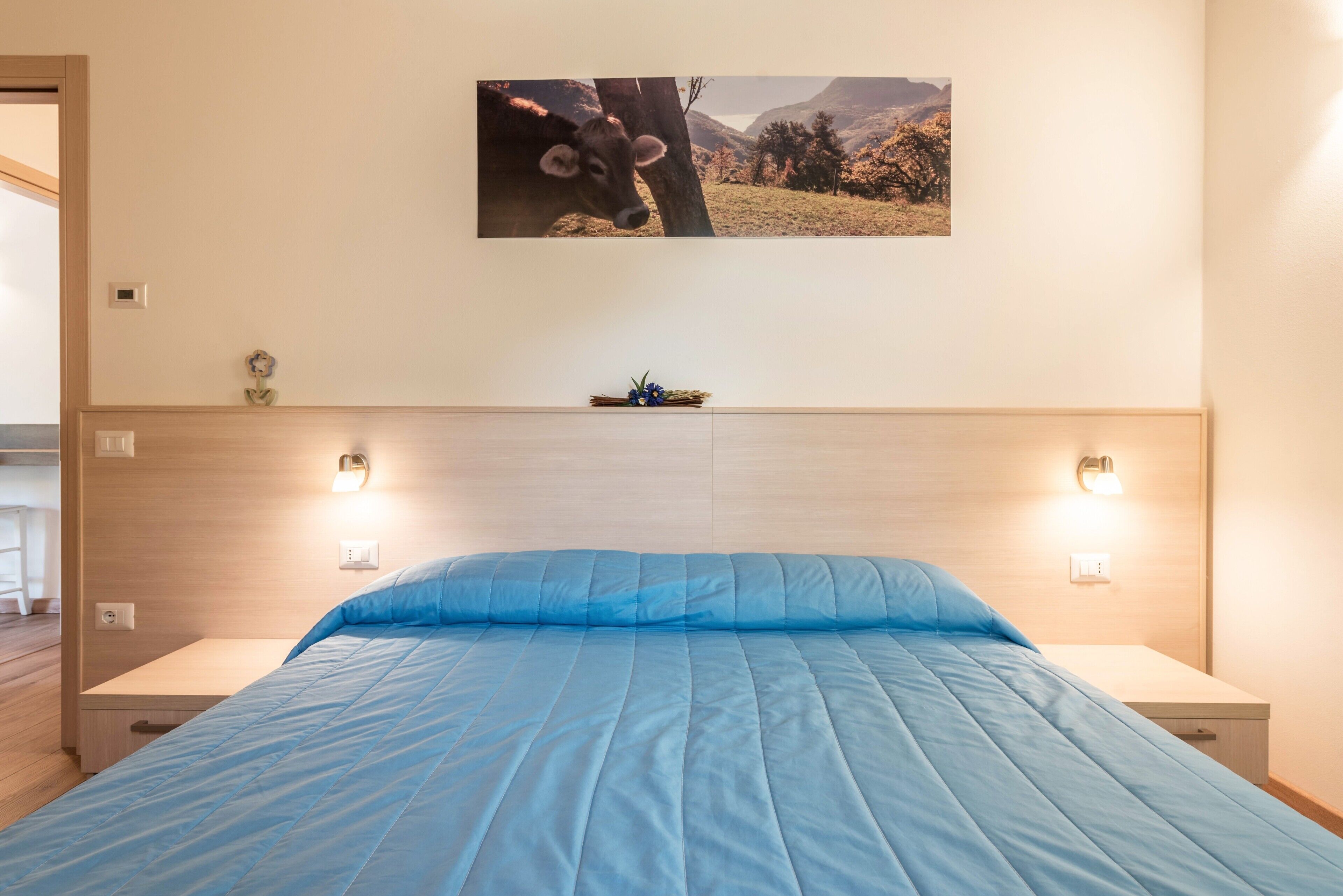 Une chambre à coucher avec un lit, des lampes de chevet, un tableau accroché au mur et une petite table sur laquelle est posé un objet décoratif.