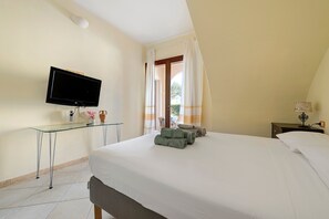 A hotel room with a bed, a TV mounted on the wall, a glass table, and a window with curtains. - Holiday Apartment "Elga" with Garden & Wi-Fi (Villasimius)
