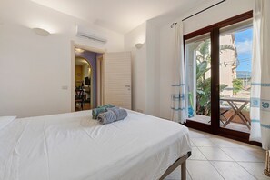 A hotel room with a bed, a door leading to a balcony, and an air conditioning unit. - Holiday Apartment "Elga" with Garden & Wi-Fi (Villasimius)