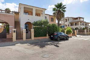 Una calle residencial con una casa de dos pisos que tiene un balcón, un automóvil estacionado adelante y una palmera.