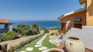 Ein Küstenanwesen mit einem Steinweg, der zu einer Terrasse führt, einem großen Terrakottatopf und Blick aufs Meer.