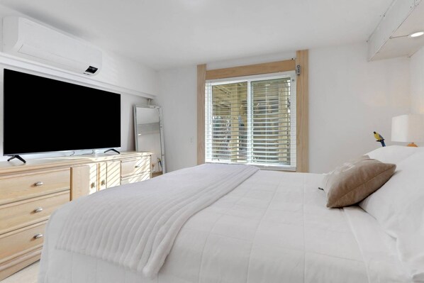 A bedroom with a bed, a TV, a dresser, and a window with blinds.